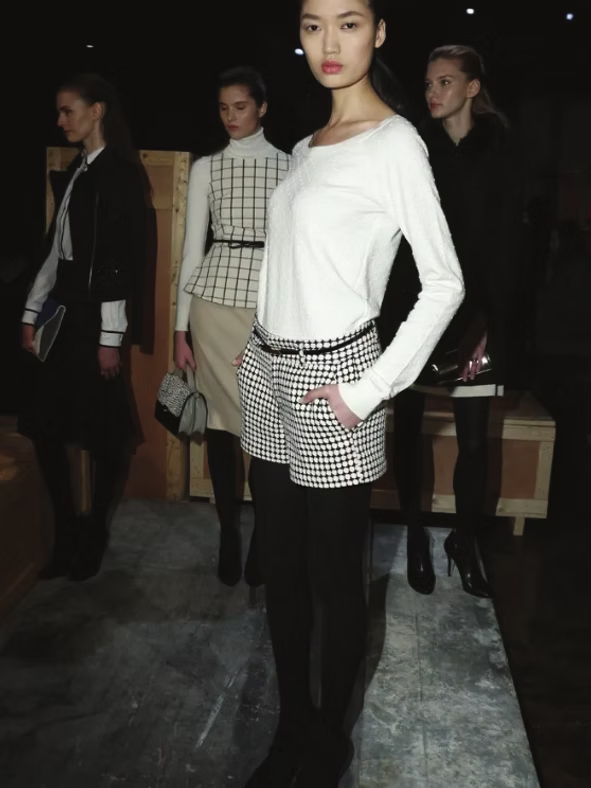 Models in black and white outfits pose indoors: shorts, blouses, jackets.