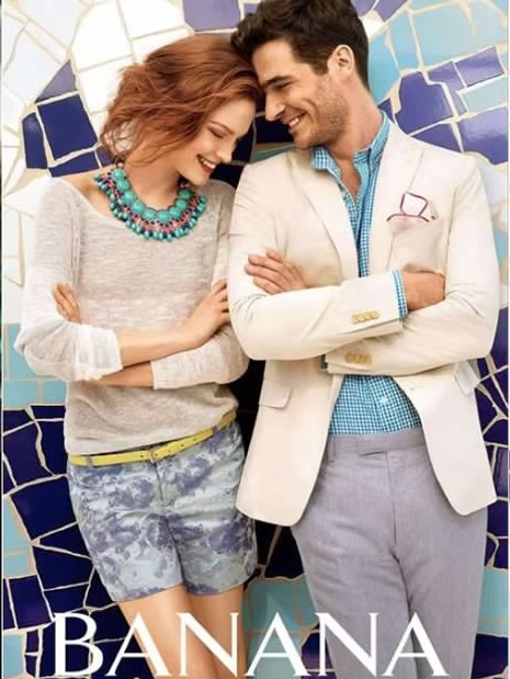 Couple leaning together, smiling. Woman in shorts, man in blazer, standing in front of blue mosaic wall. Banana Republic ad.