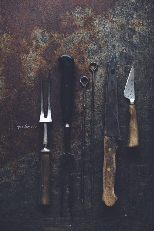 Collection of vintage, weathered cooking utensils on a rusty metal surface.