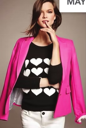 Woman in pink blazer, black sweater with white hearts, and white pants, looking at the viewer.