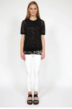 Woman wearing black lace top, white jeans, black sandals. Standing in front of a white background.