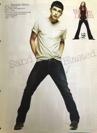 Man in white shirt and jeans with hands in pockets; poses in studio.