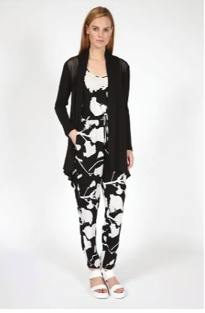 Woman wearing a black cardigan over a black and white jumpsuit and white sandals.