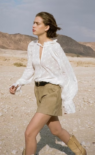 Woman in white top and brown shorts walking outdoors.