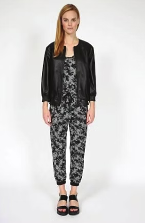 Woman in black jacket, floral jumpsuit, and sandals, standing.