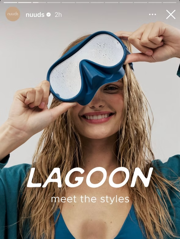 Woman holding a blue sleep mask over her eyes, smiling. 