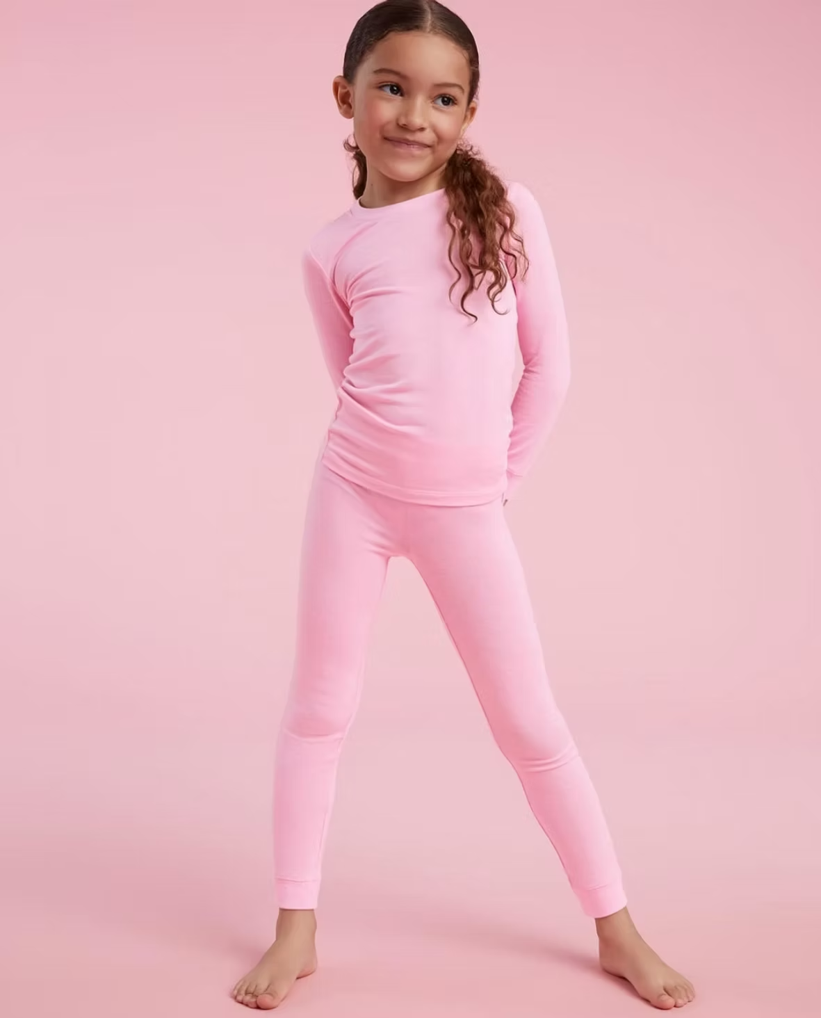 Girl in pink pajamas poses smiling against a pink backdrop.
