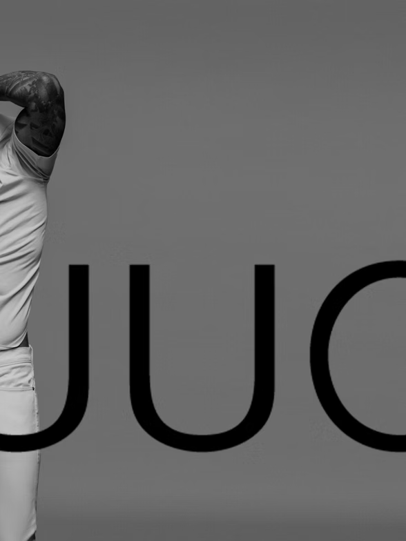 Man in light clothing with tattooed arm, partially obscured by the word 