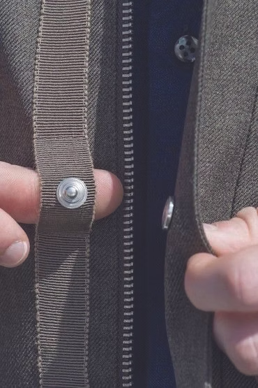 Hands fastening a brown jacket with snaps and a zipper.