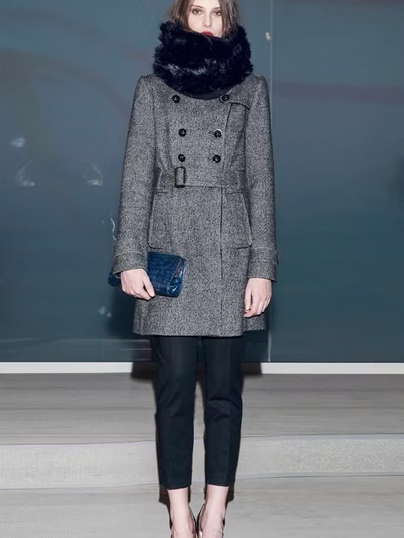 Woman in gray coat, black pants, and fur scarf, holding a blue clutch.