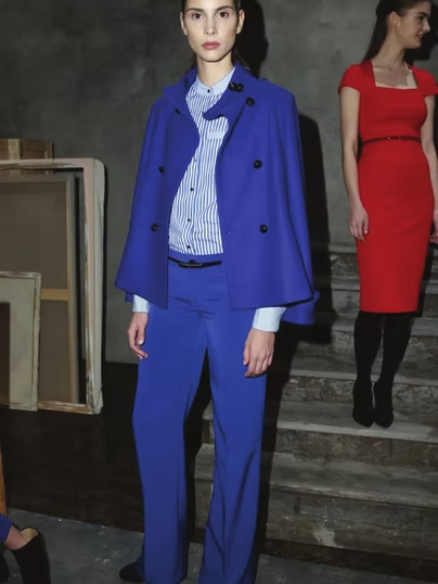Woman in blue suit and cape, standing on steps, another woman in red dress.