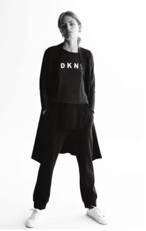 Woman in black DKNY sweatsuit and cardigan, hands in pockets, posing.