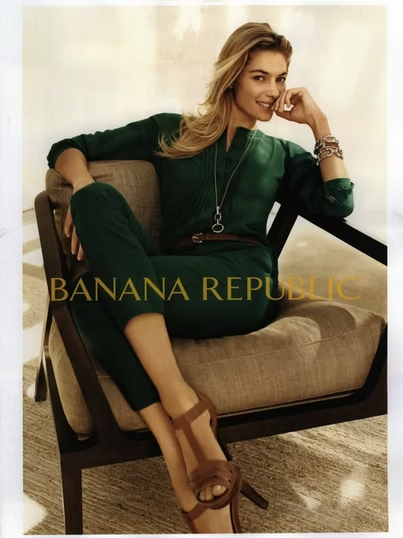 Woman in green outfit sits in a chair, smiling, advertising Banana Republic.