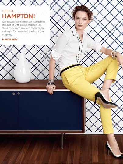 Woman in yellow pants and white shirt, posing on a blue cabinet, against a diamond pattern backdrop.