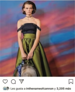 Woman in off-the-shoulder dress holds a round, metallic object, posing in front of a colorful backdrop.