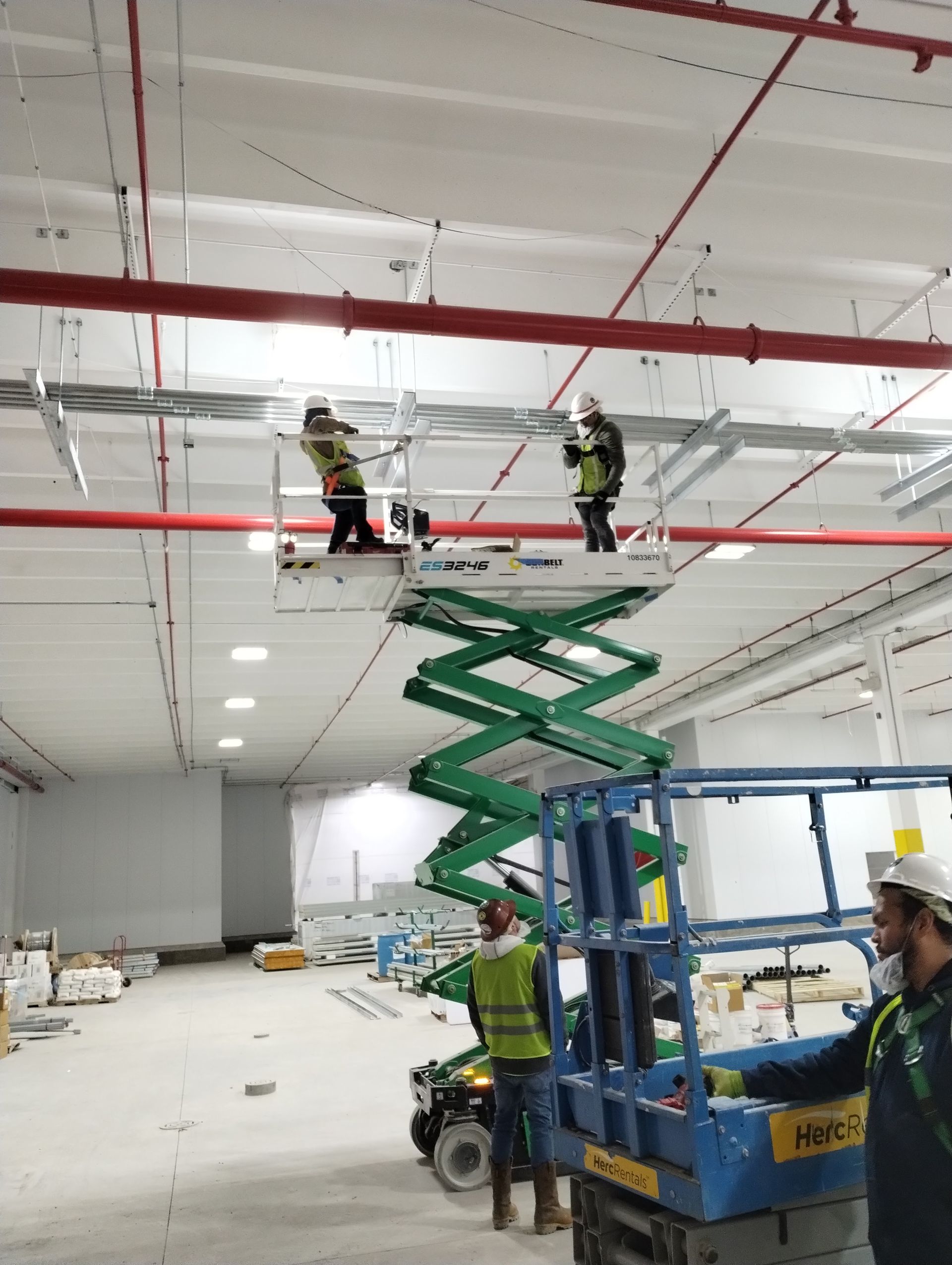 Two workers on a scissor lift installing wiring, another worker on the ground. Warehouse interior.