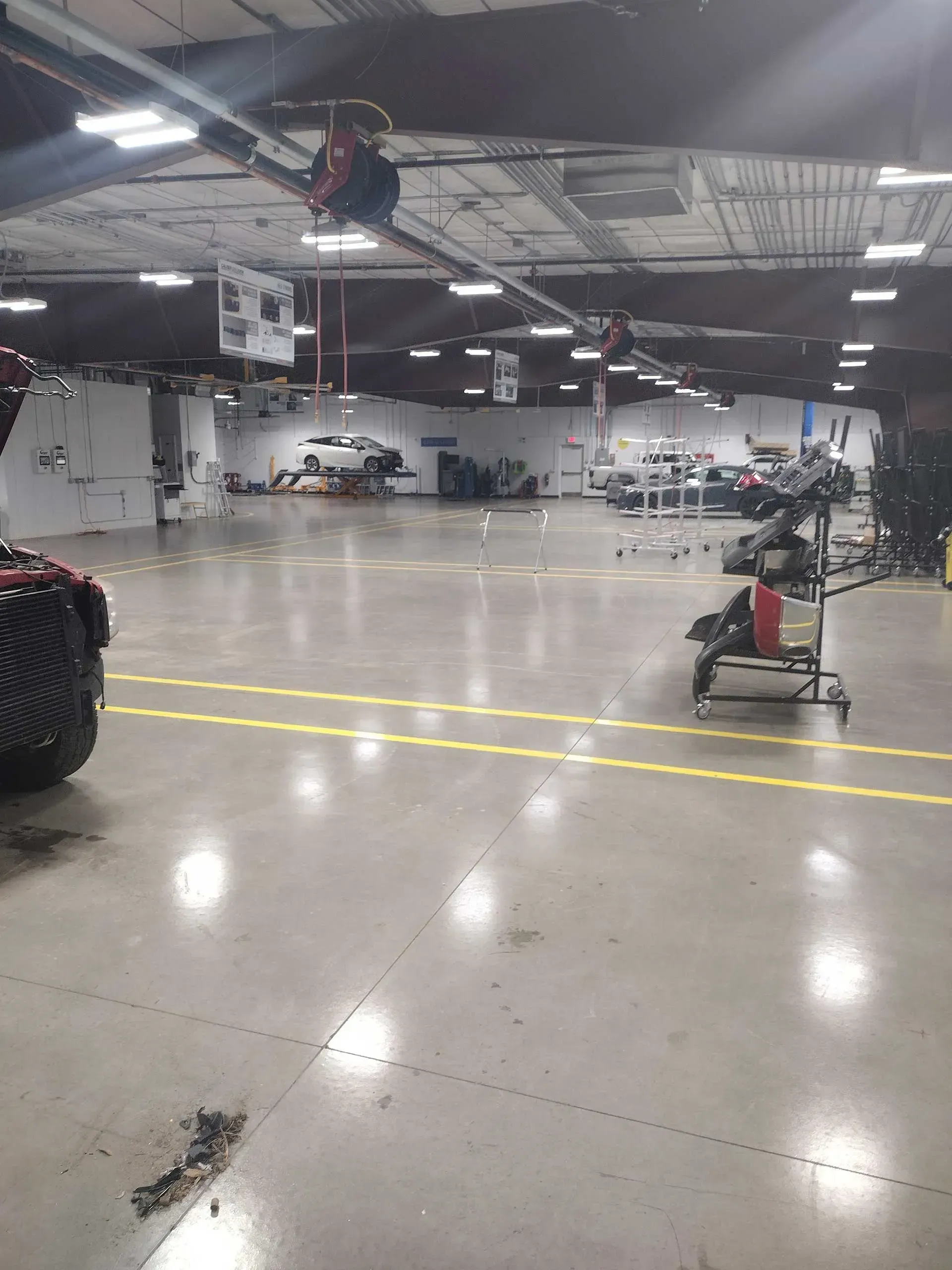 Large auto repair shop with cars, tools, and overhead equipment. Gray floor, white walls, red accents.