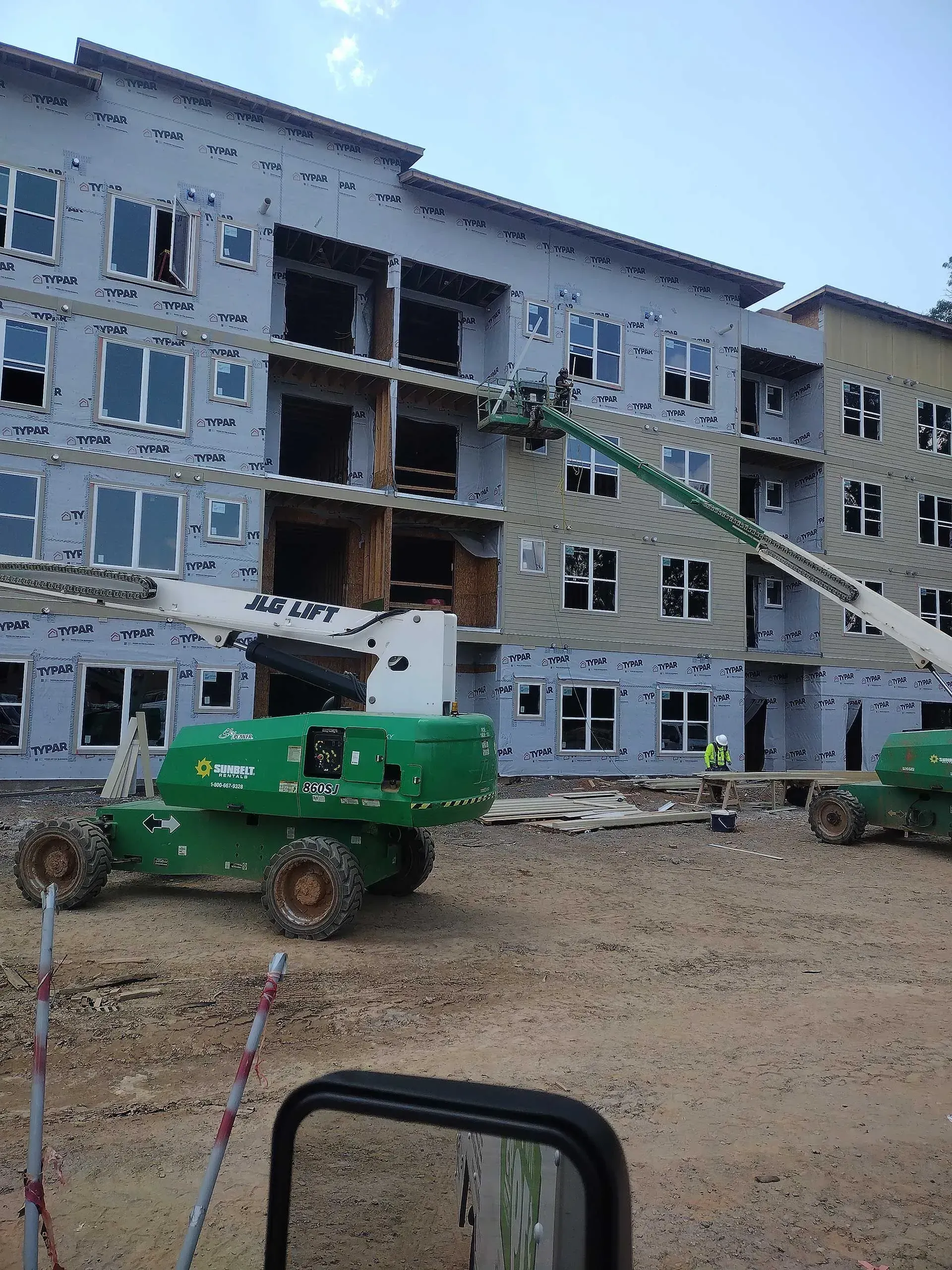 Construction site with green machinery, building with windows, workers.