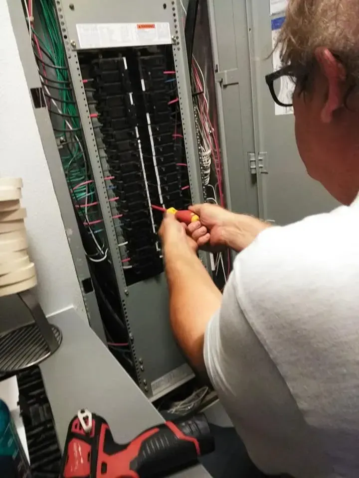 Electrician working on a circuit breaker panel with a screwdriver, indoors.