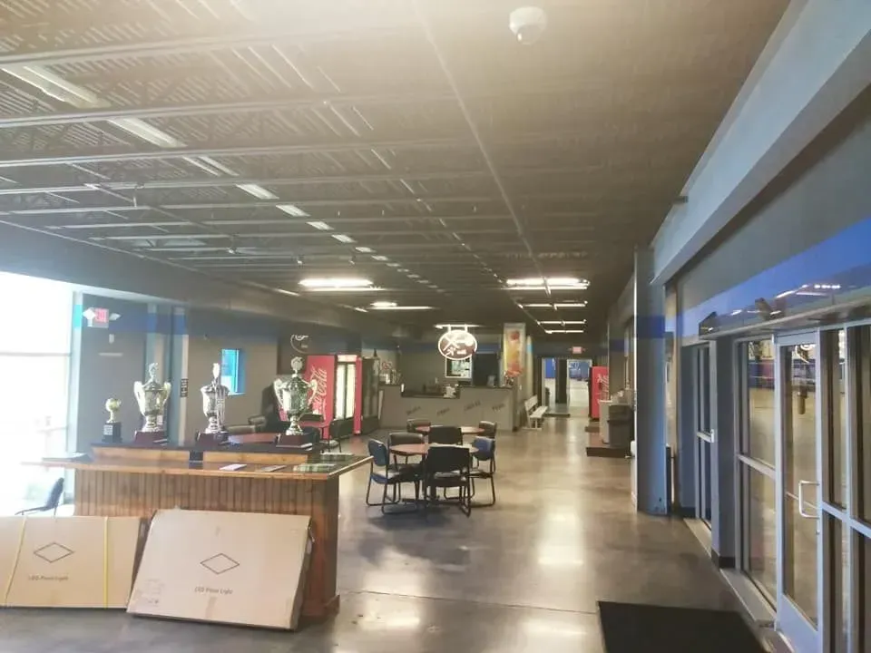 Hallway with trophies, tables, and posters; grey ceiling and floor, bright doorway.
