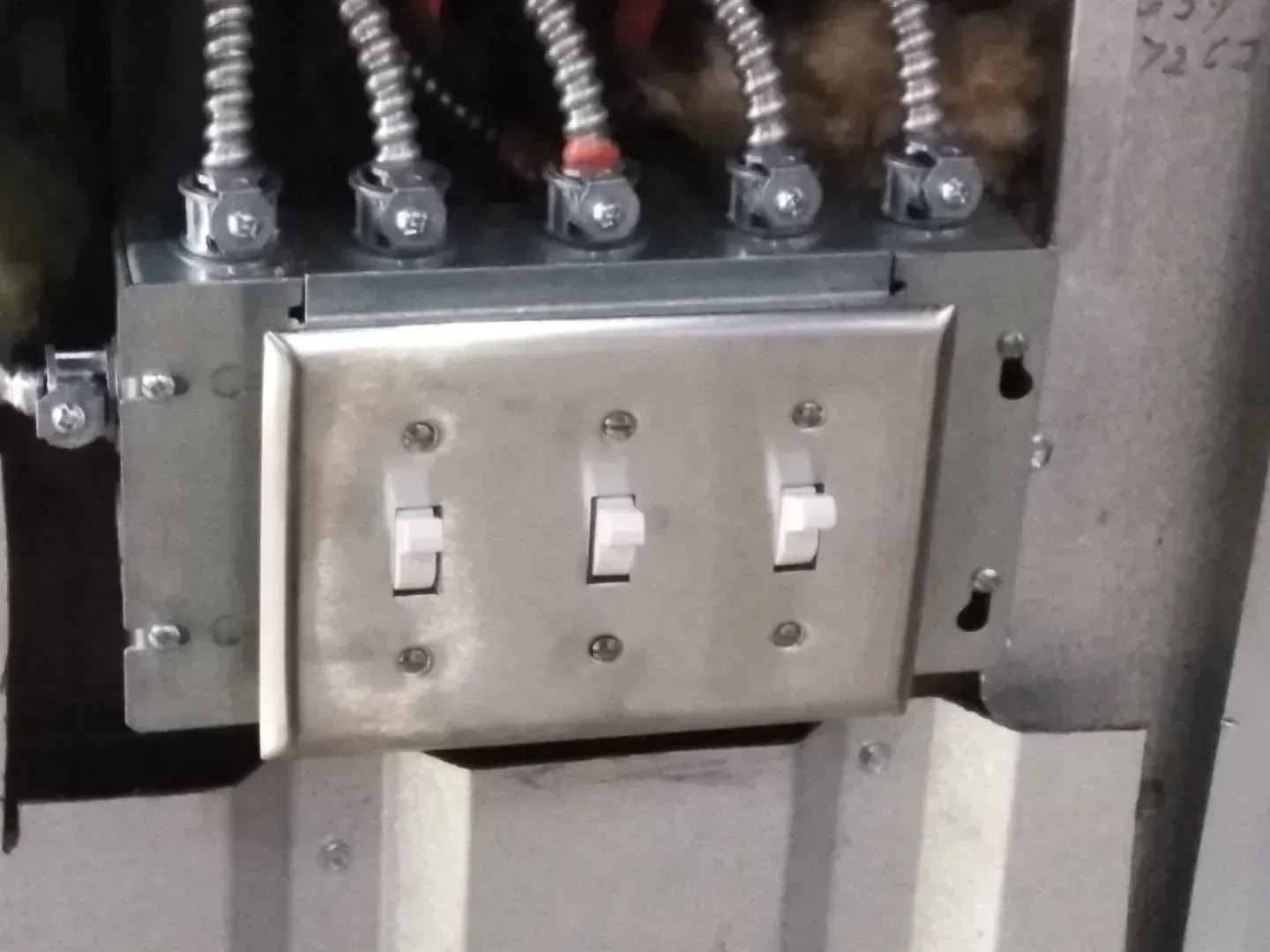 Metal electrical box with three light switches and wiring.
