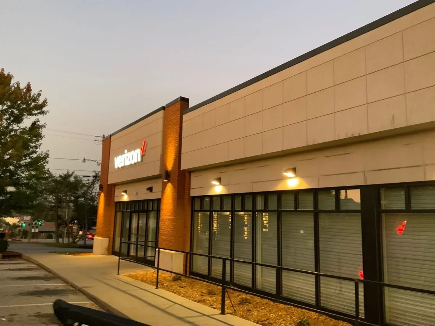 Verizon store with lit sign, brick pillars, and windows along a sidewalk.