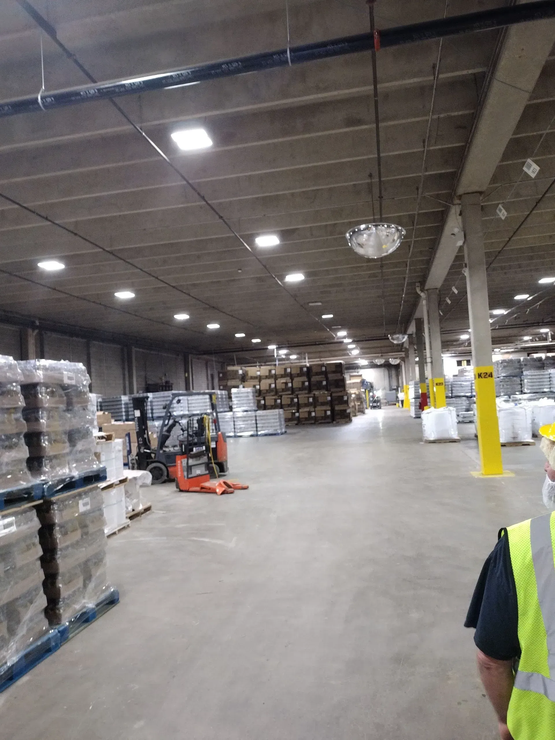 Warehouse interior with pallets of goods, a forklift, and person wearing a safety vest.