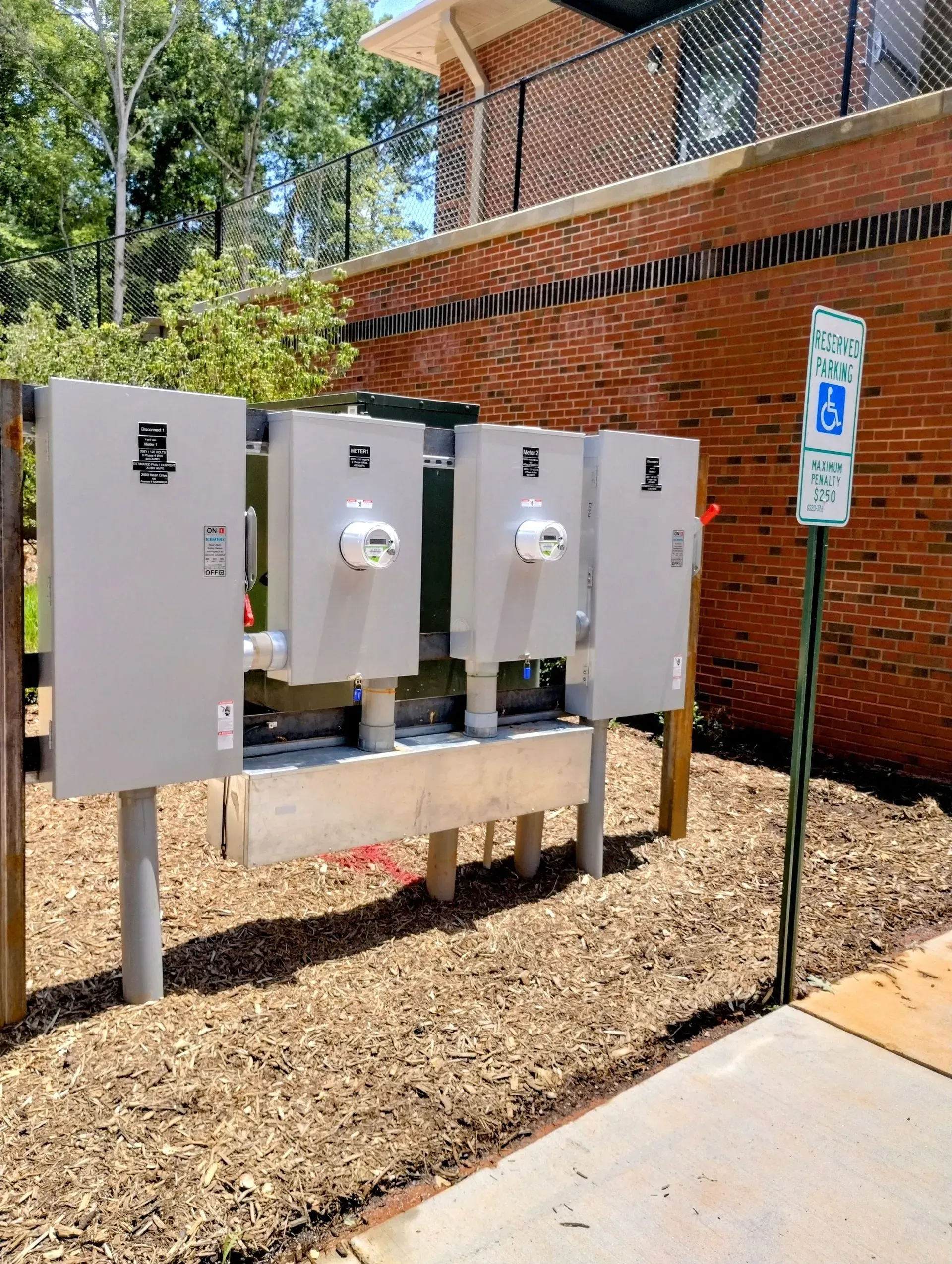 Electrical boxes with meters, in front of a brick wall, with a handicap parking sign.