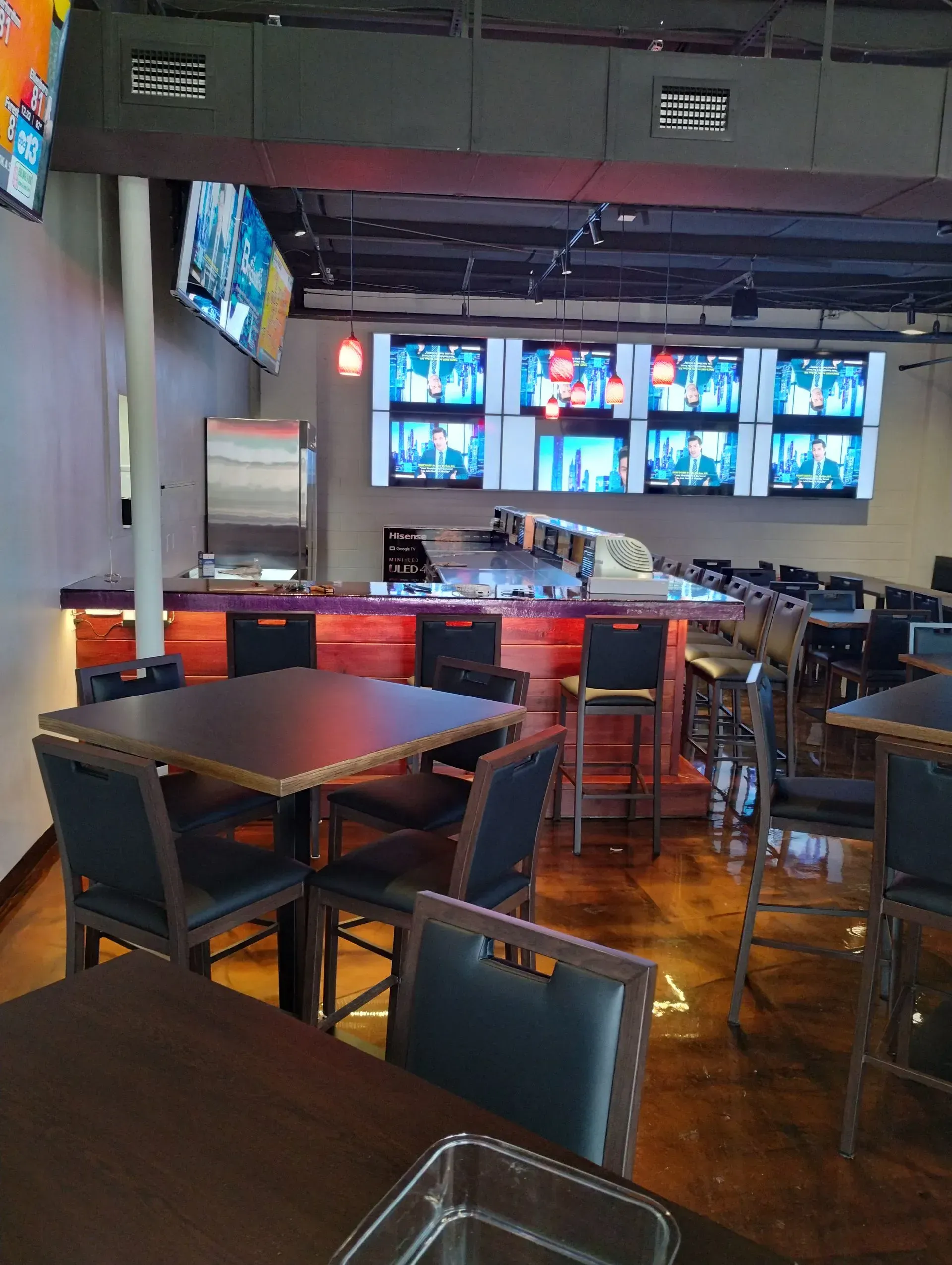 Interior of a sports bar with TVs, a bar, tables, and chairs. Dim lighting.