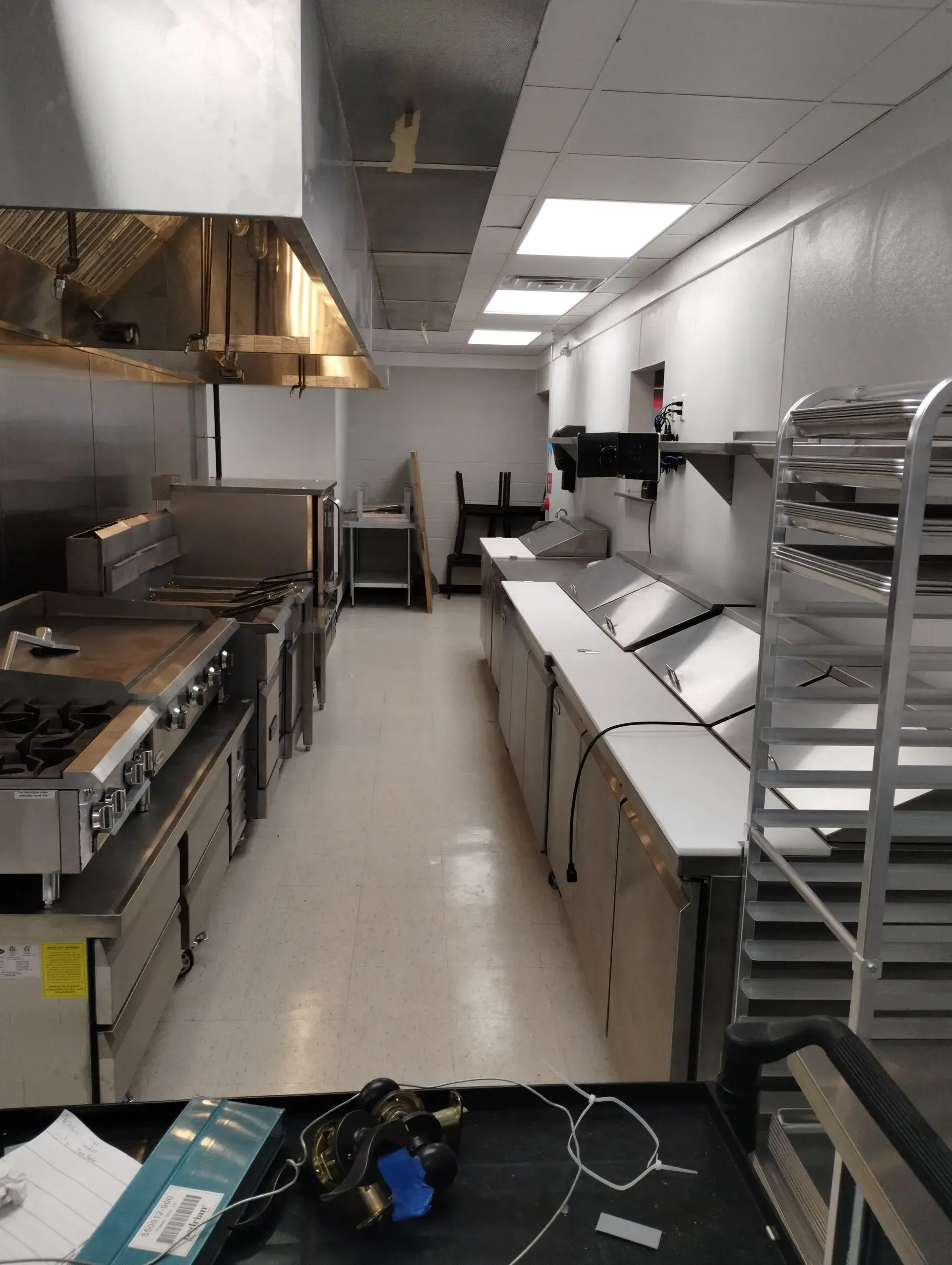 Narrow commercial kitchen with stainless steel equipment and white countertops, viewed from the entrance.