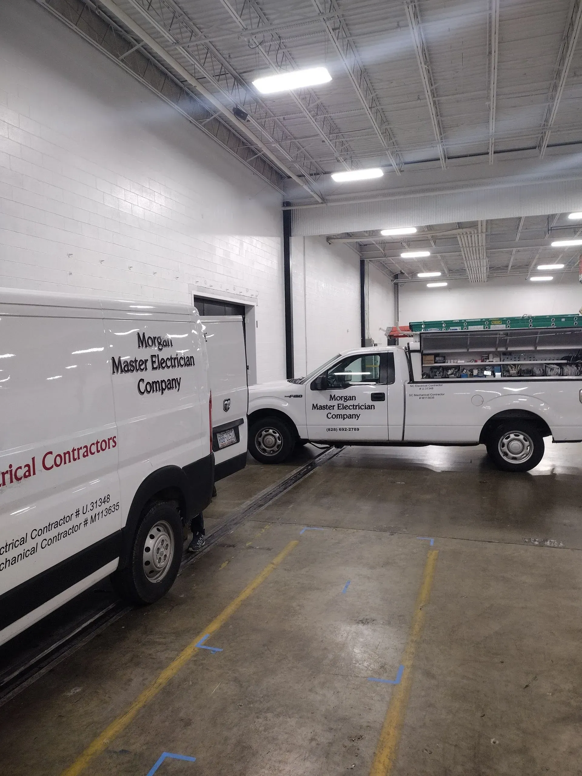 Two white work trucks parked inside a warehouse; one has the text 