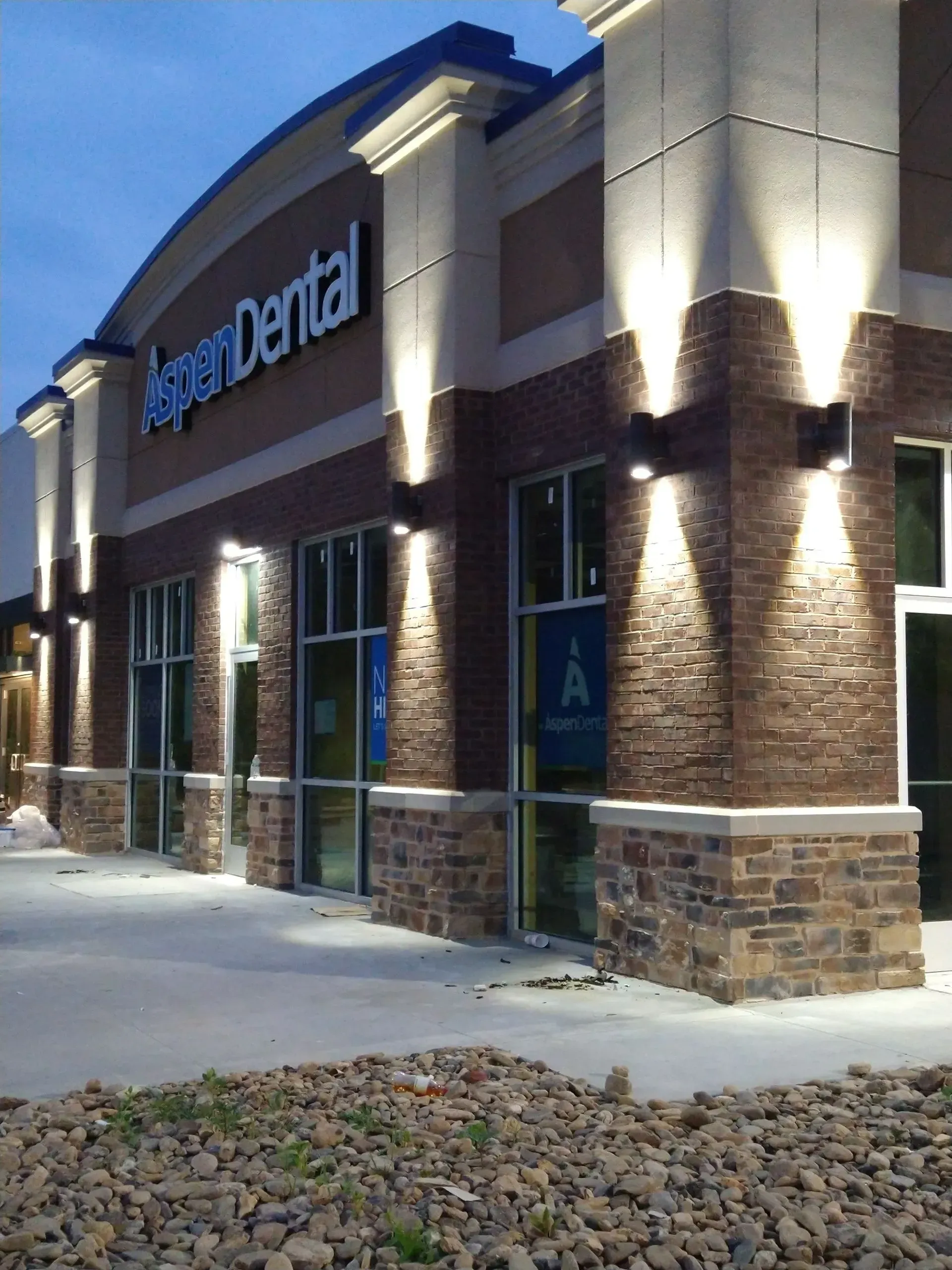 Exterior of Aspen Dental at dusk, with illuminated brick facade and signage.