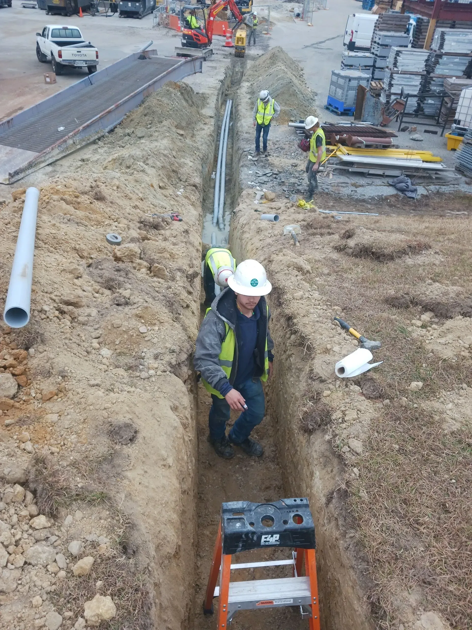 Construction workers installing pipes in a trench at a work site.