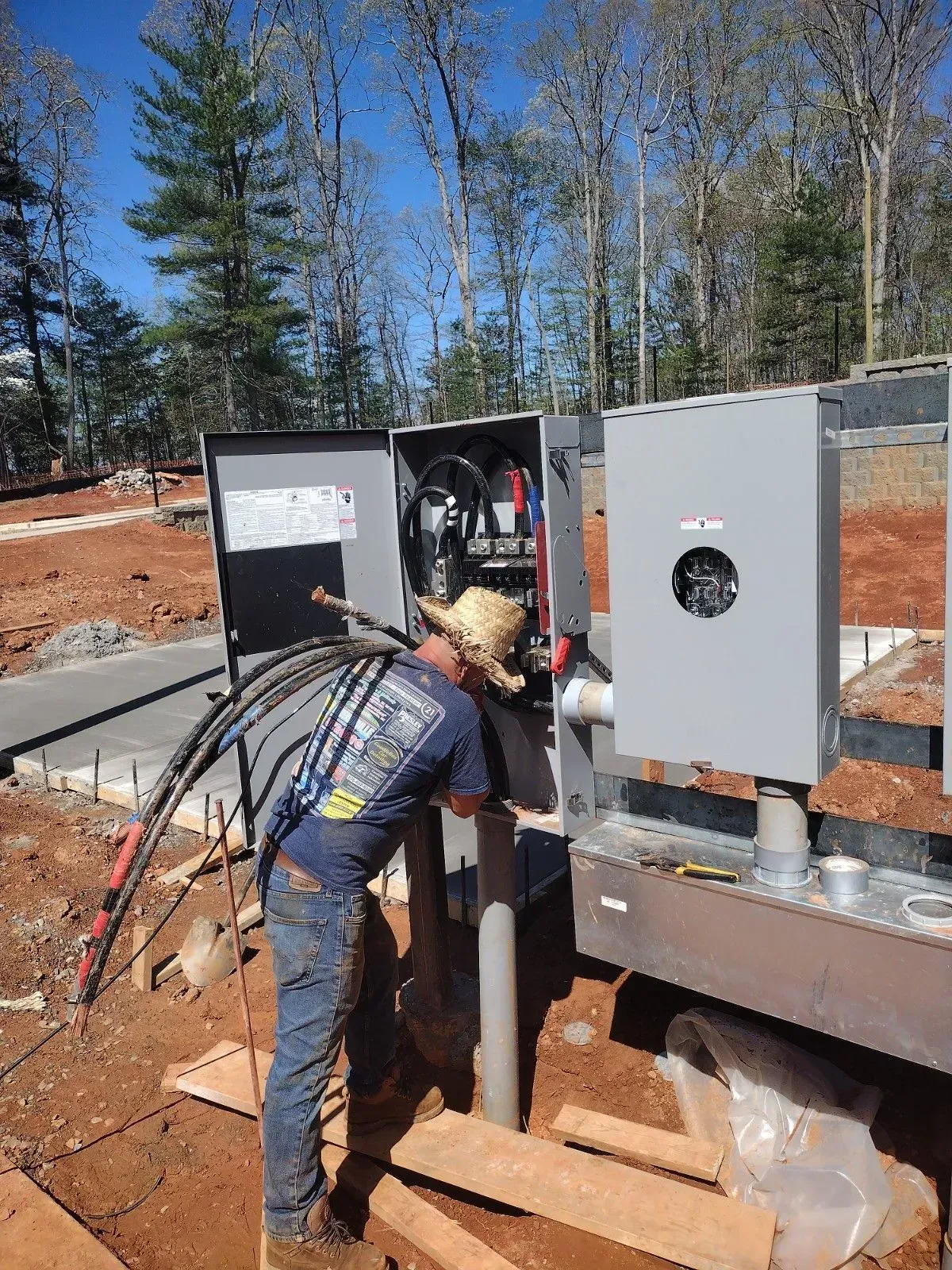 Electrician working on electrical panel outdoors, wearing a straw hat.