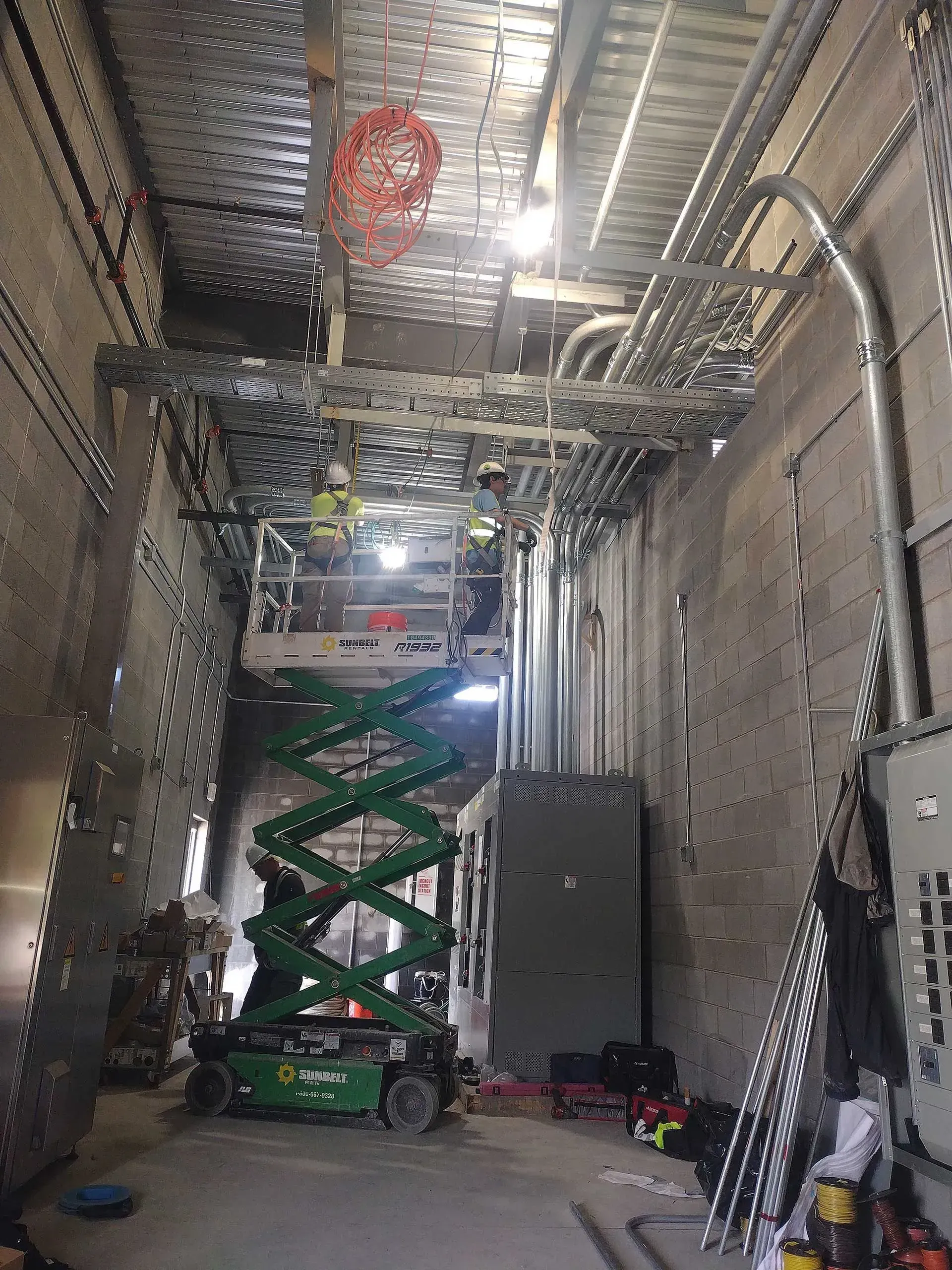 Construction site with a scissor lift, electrical conduits, and a worker; gray and silver tones.