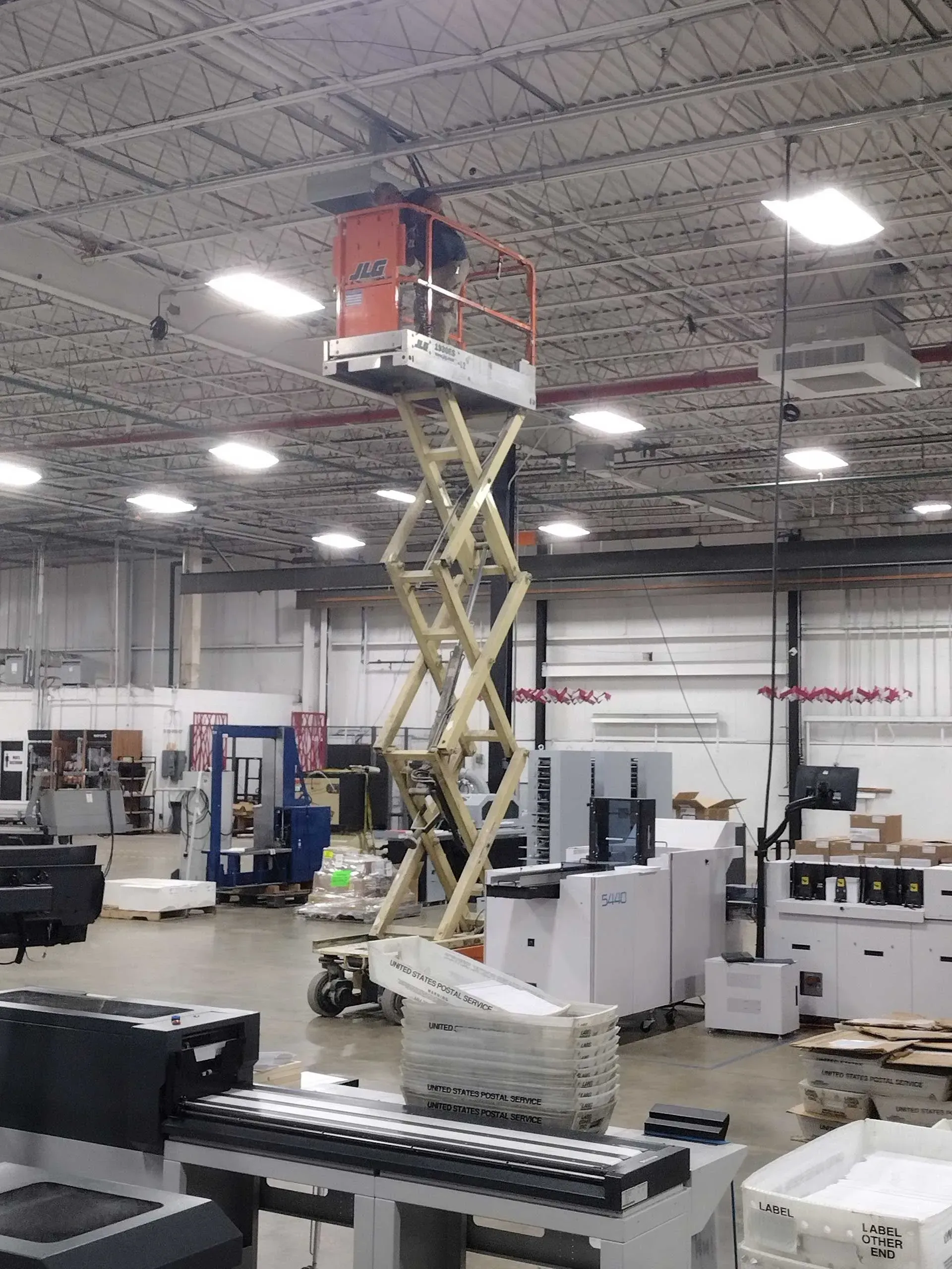 A person operates a scissor lift in a large warehouse.