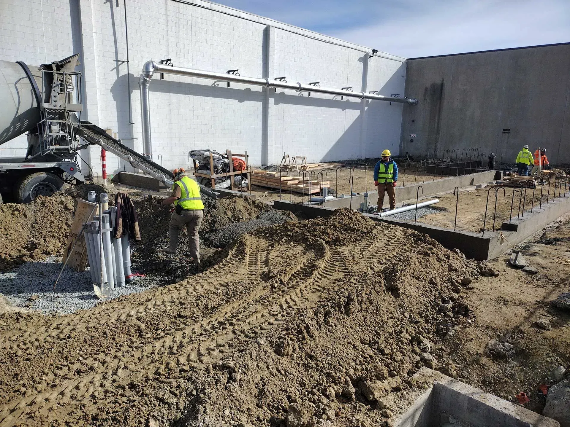 Construction workers pouring concrete for a foundation outside a large building.