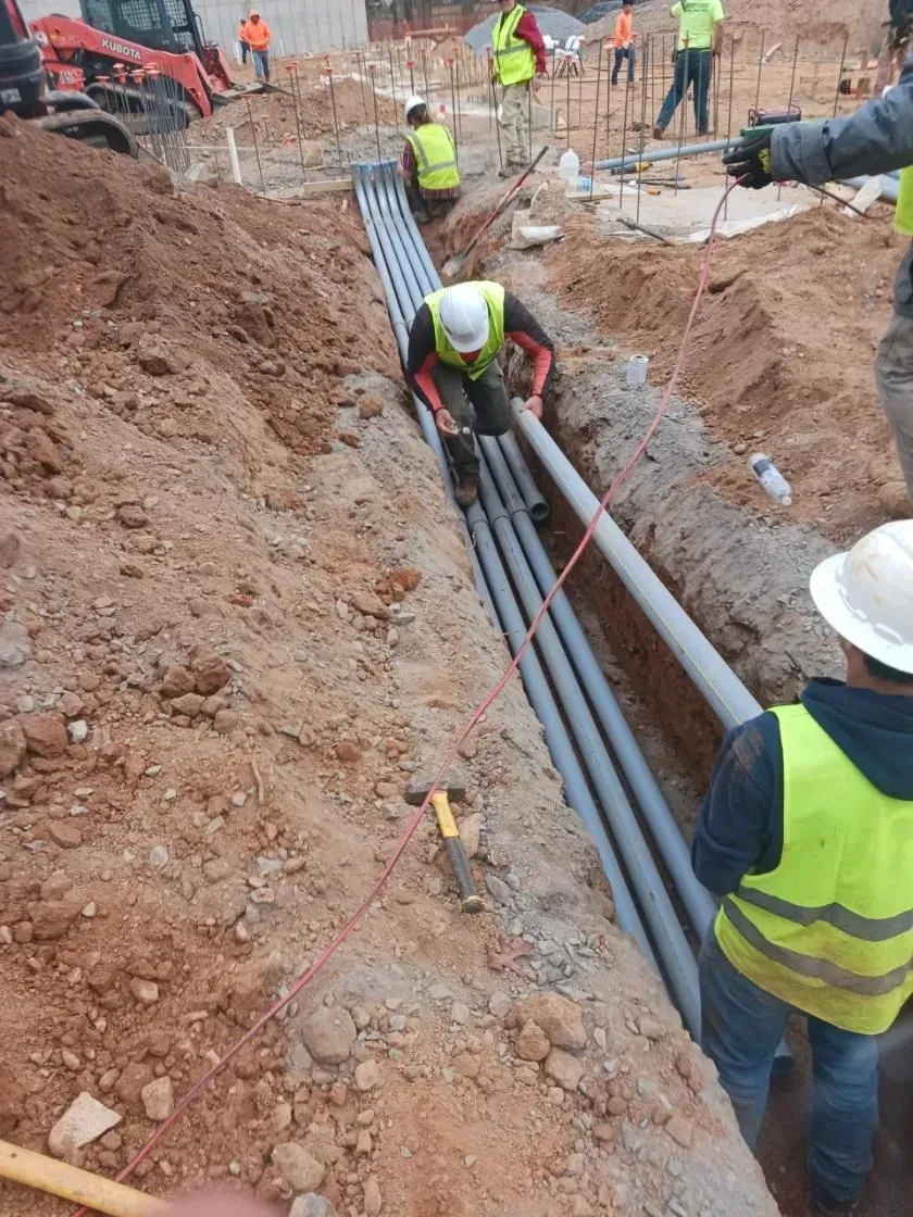 Construction workers installing gray pipes in a trench at a construction site.