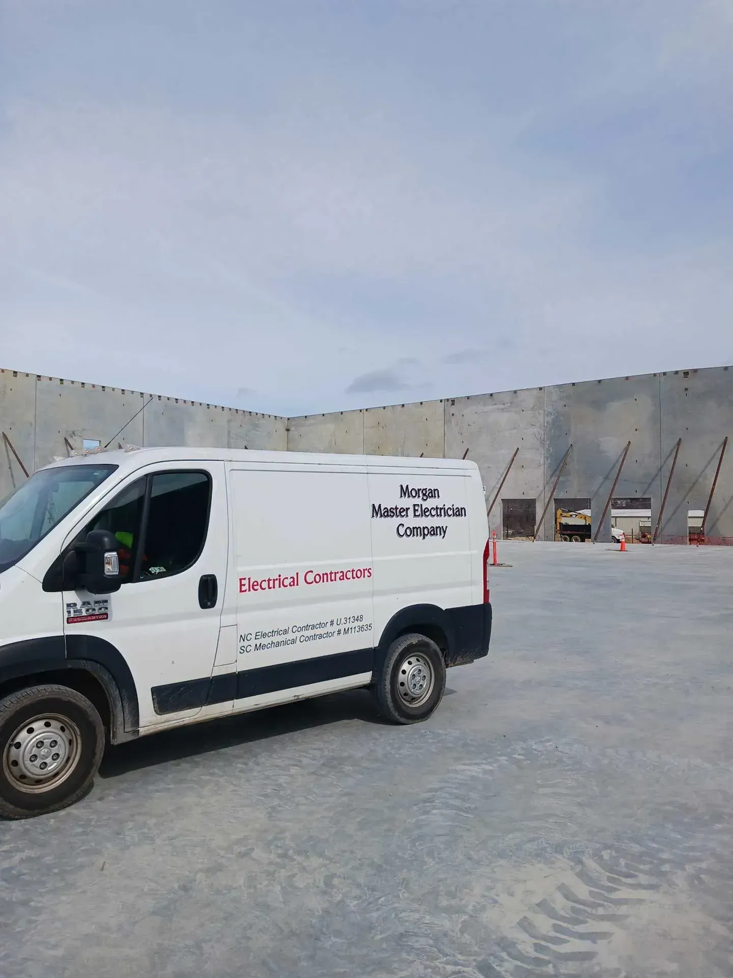 White work van with company logo parked in front of concrete building under cloudy sky.