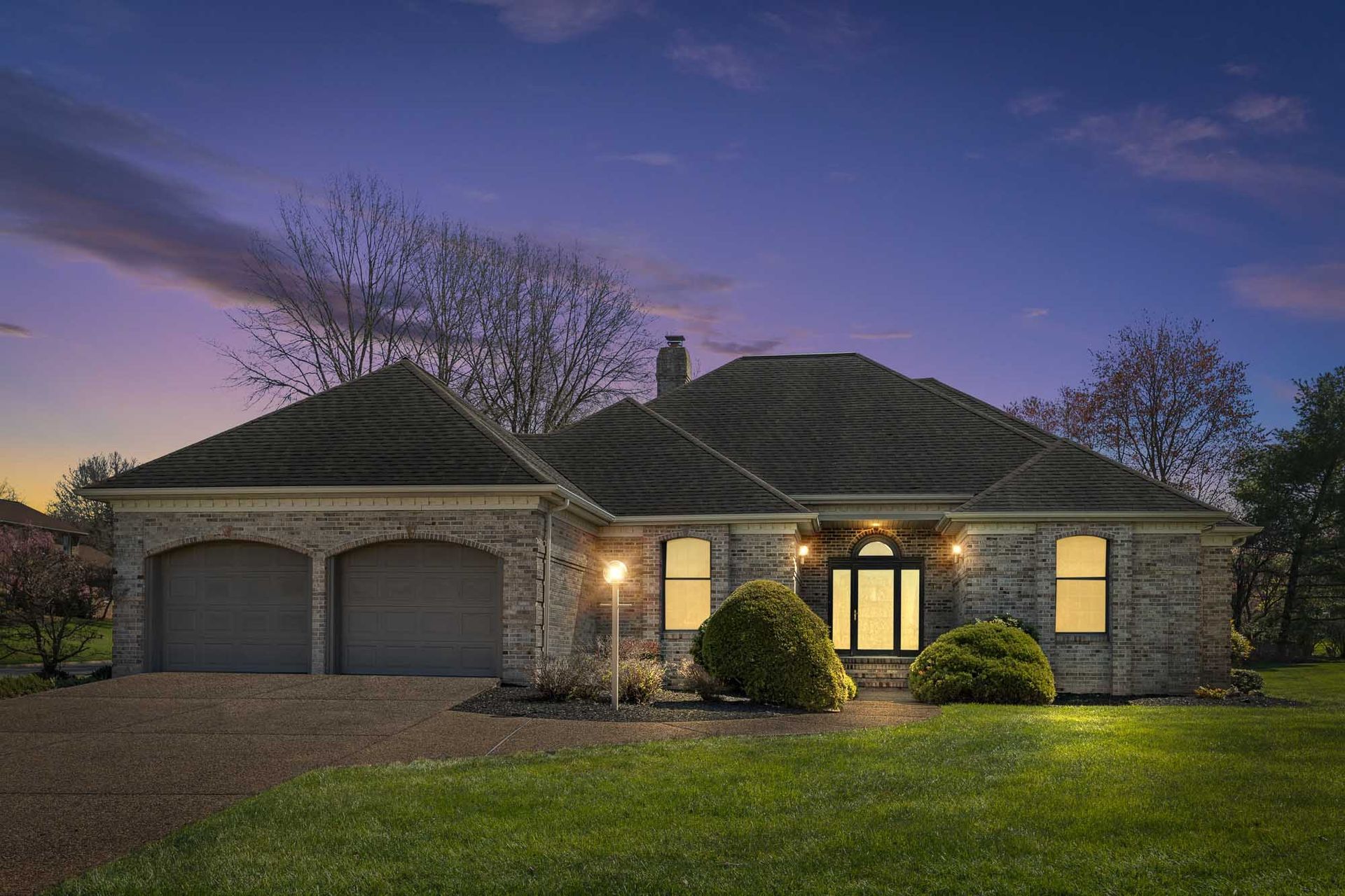 A large brick house with two garages is lit up at night.