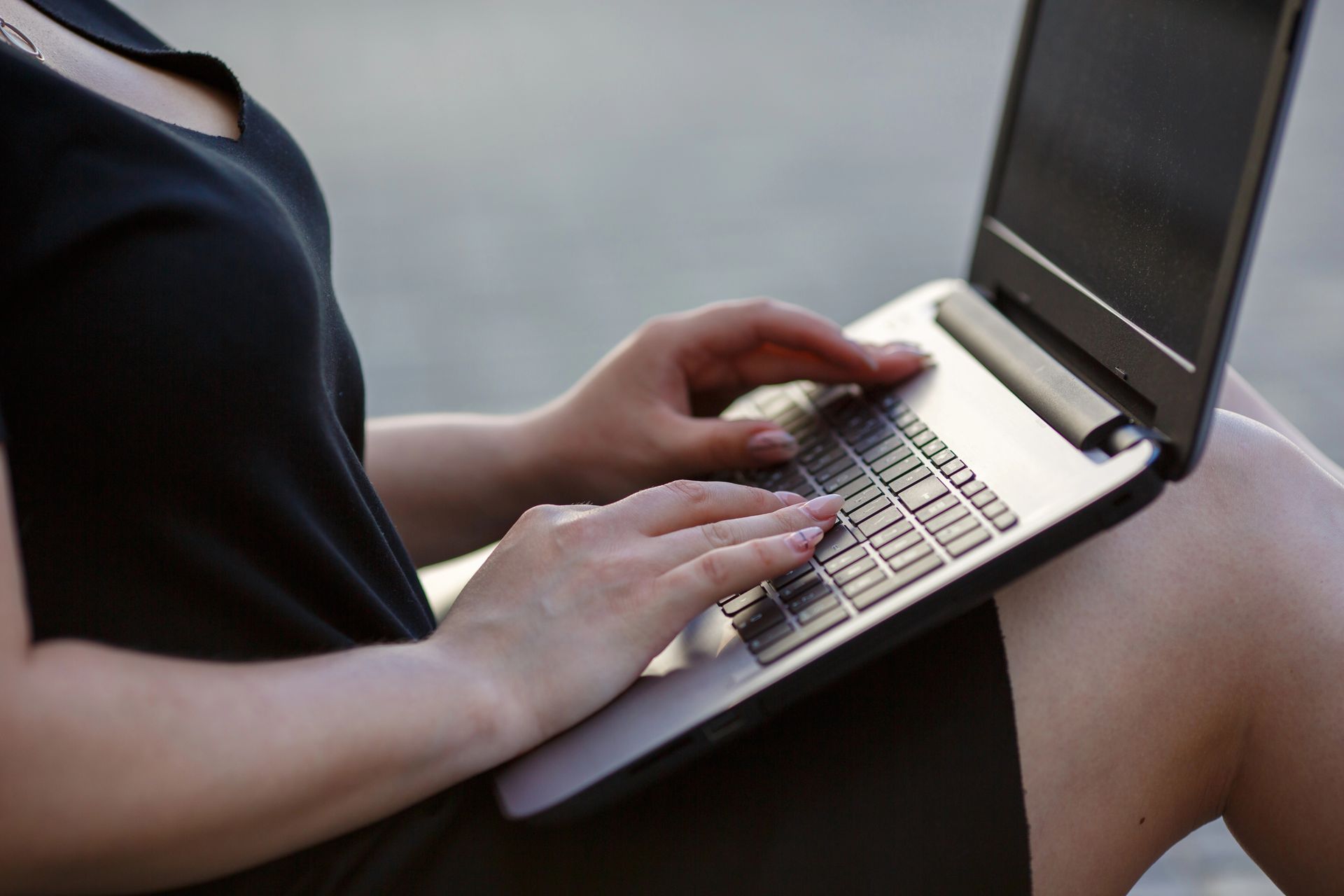 Woman in black dress typing on a laptop, outdoors.