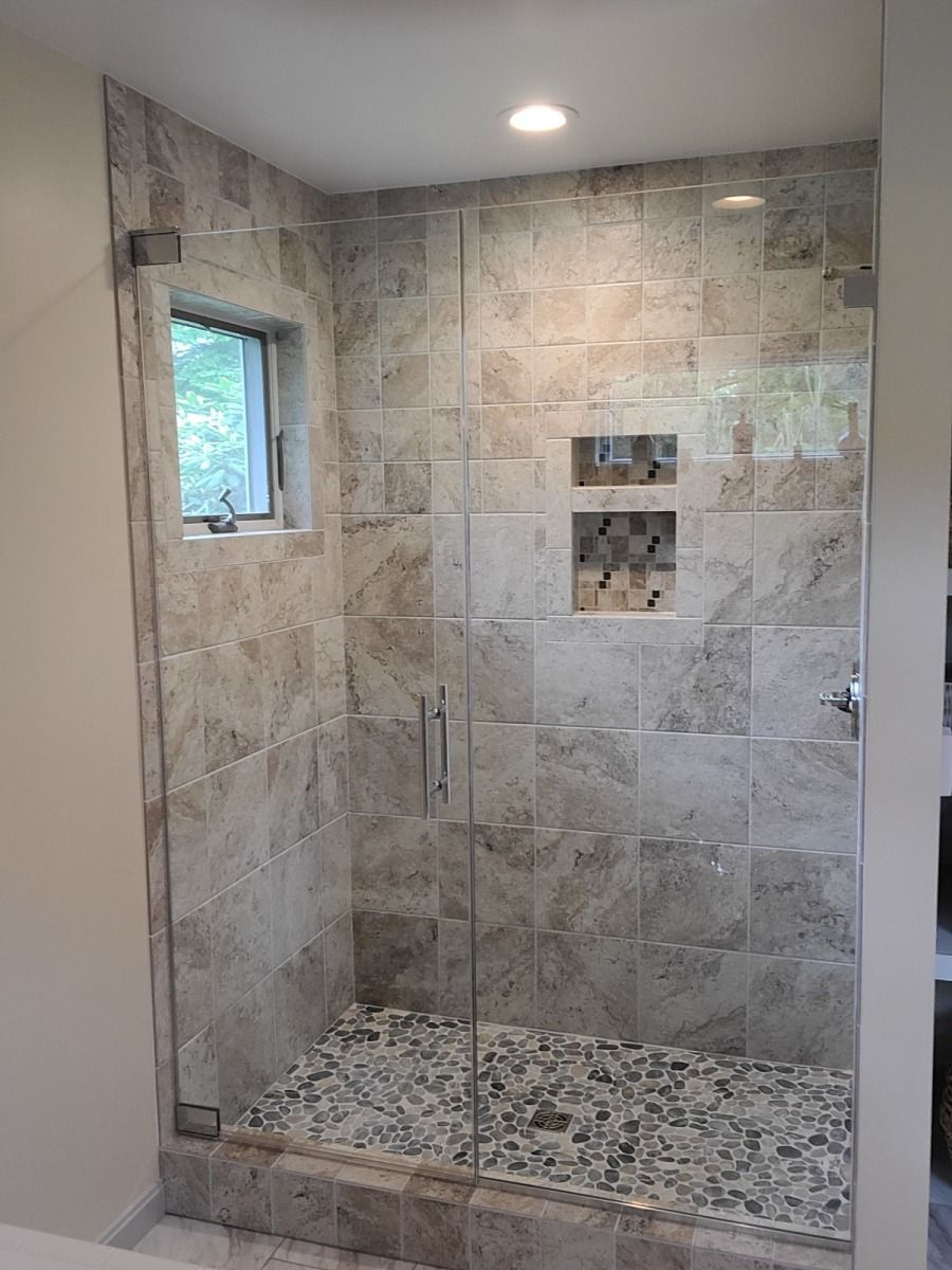 A bathroom with a walk in shower with a glass door and a window.