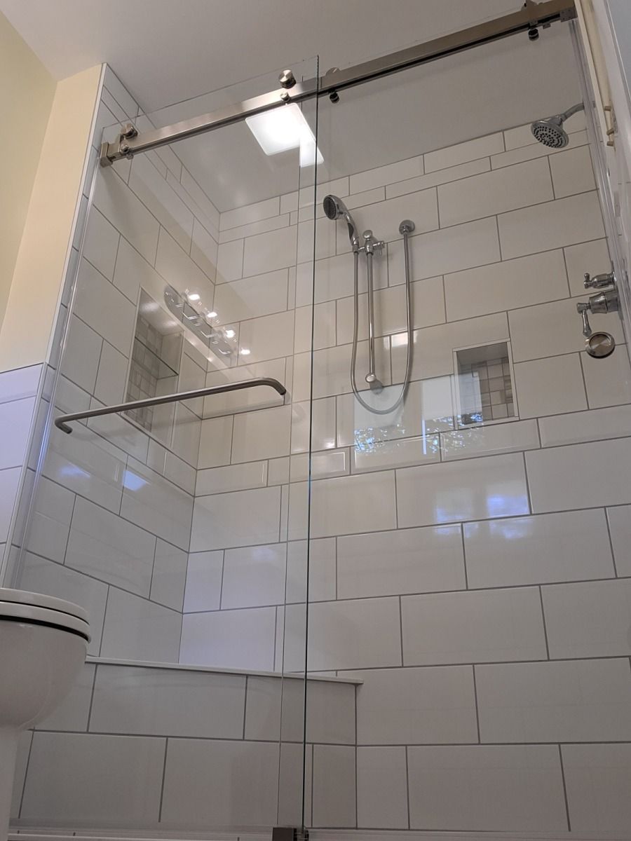 A bathroom with white tiles and a sliding glass shower door.