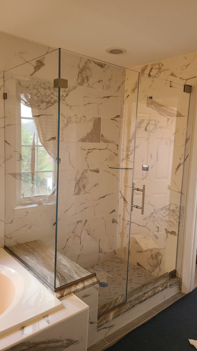 A bathroom with marble walls and a walk in shower with a glass door.