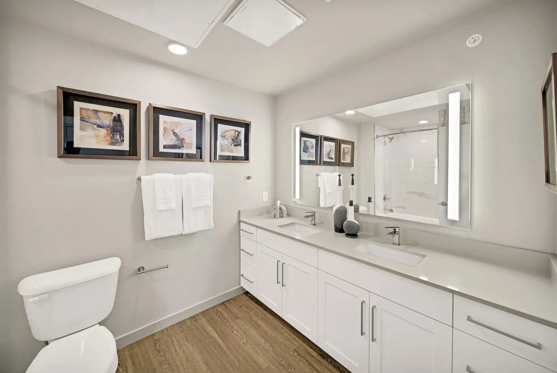 Modern bathroom with a double vanity, large illuminated mirror, and a toilet.