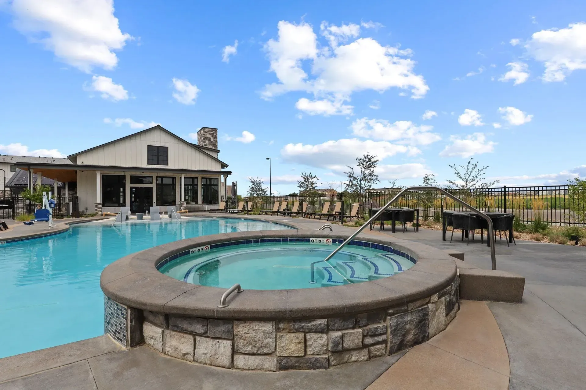 Outdoor swimming pool and hot tub with lounge chairs and tables.