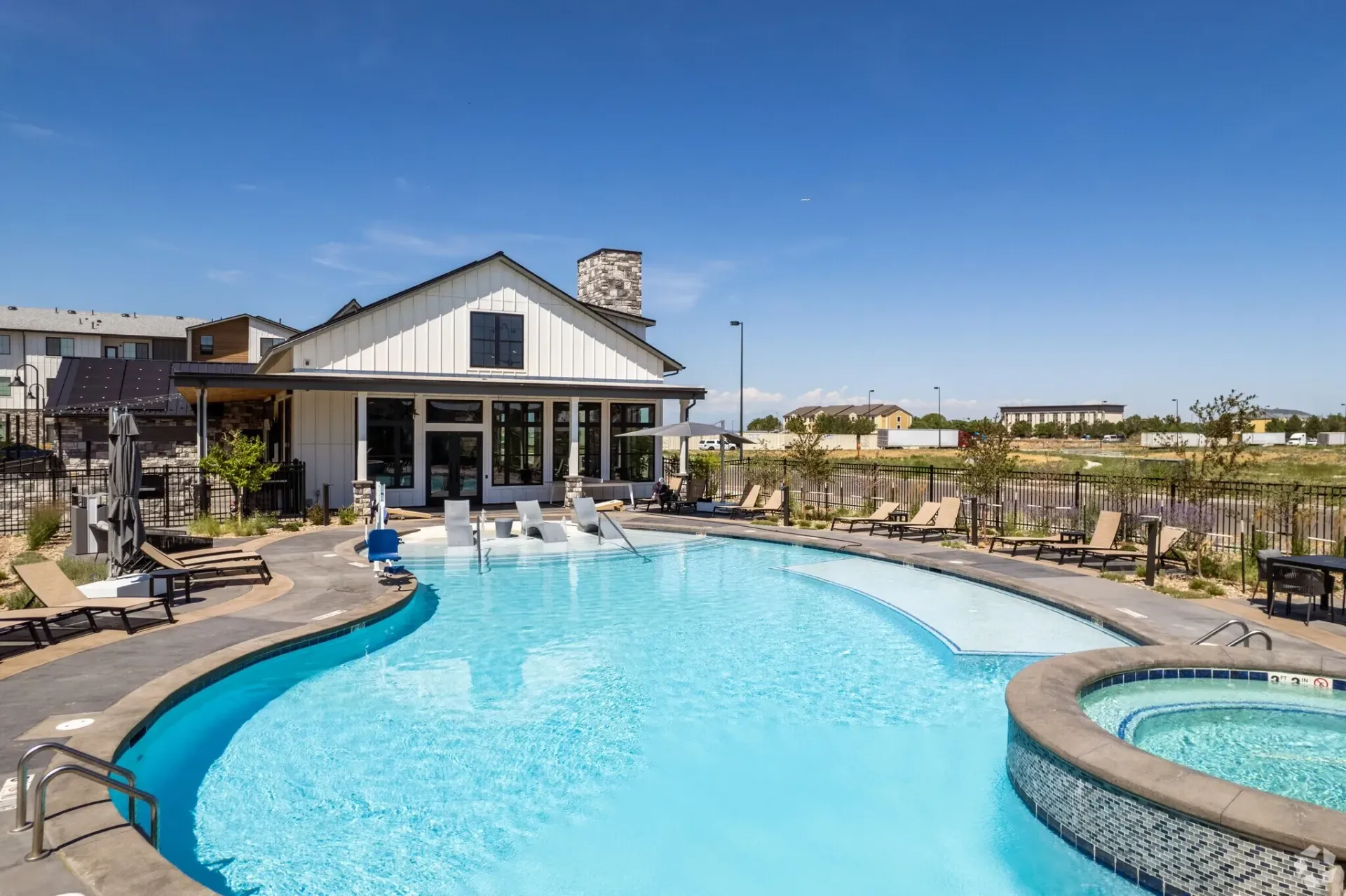 Resort-style swimming pool with loungers and a spa adjacent to a modern clubhouse.