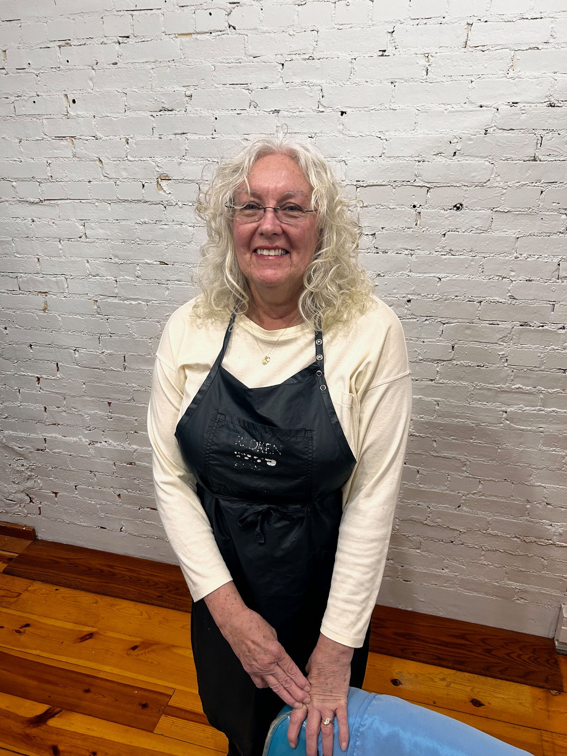 a woman wearing an apron and glasses is standing in front of a white brick wall .