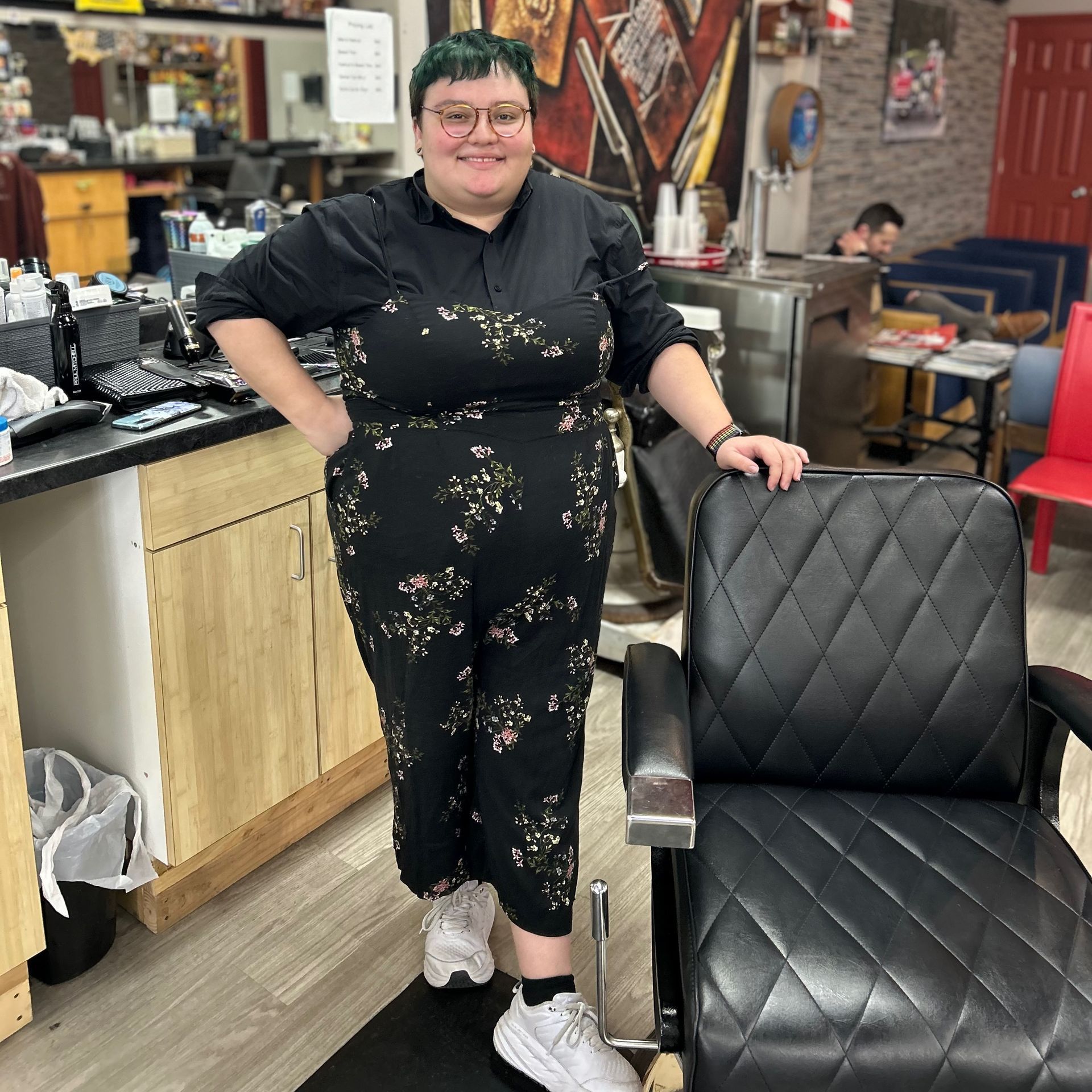 a woman in a black jumpsuit is standing next to a black chair