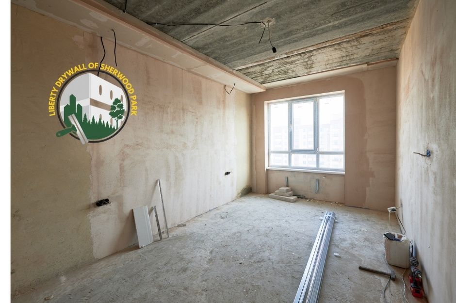 Sheetrock installation before photo showing a bare, unfinished residential room with an exposed concrete ceiling, unpainted drywall, scattered construction tools, and metal studs on the floor in Sherwood Park, Alberta.